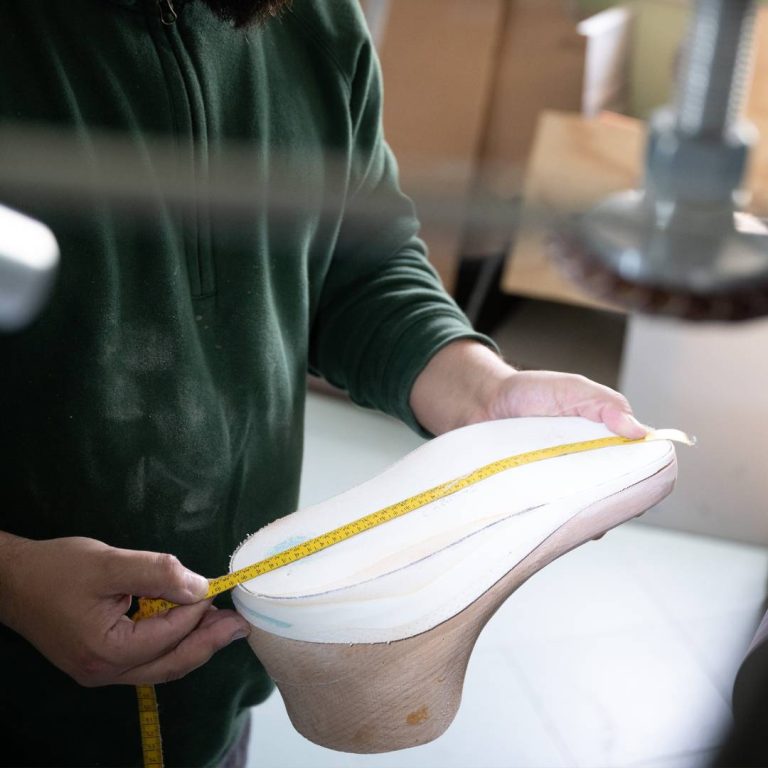 Tecnico ortopedico che misura una forma in legno per la realizzazione di scarpe su misura