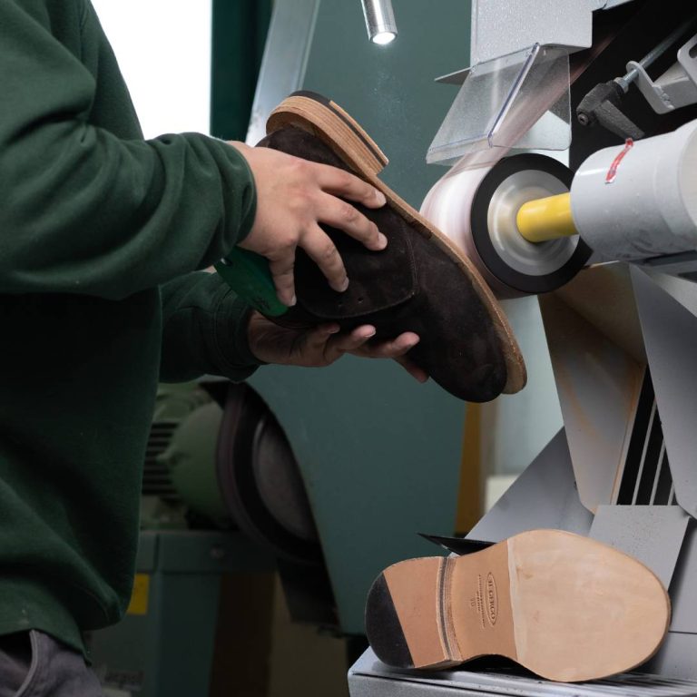 Tecnico ortopedico che rifinisce scarpe su misura con una smerigliatrice per fondo scarpe a tampone